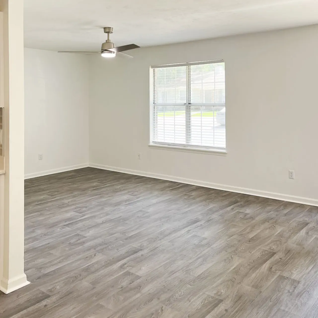Spacious living room with light-colored walls and large window, modern light fixture, and laminate flooring.