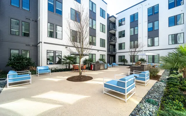 A view of a modern apartment courtyard featuring various seating arrangements, a central tree, and landscaping.