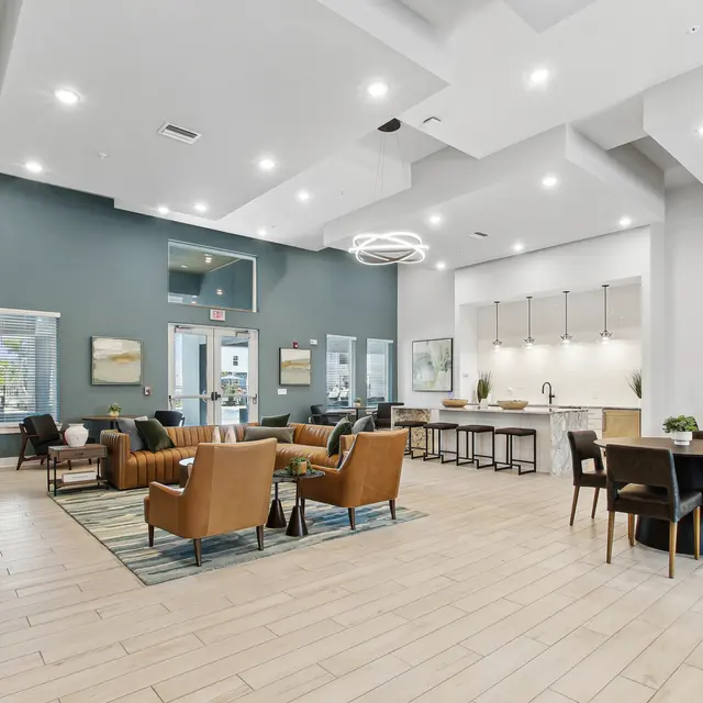 Modern common area with seating, a dining space, and a kitchen, featuring blue accents and ample natural light.