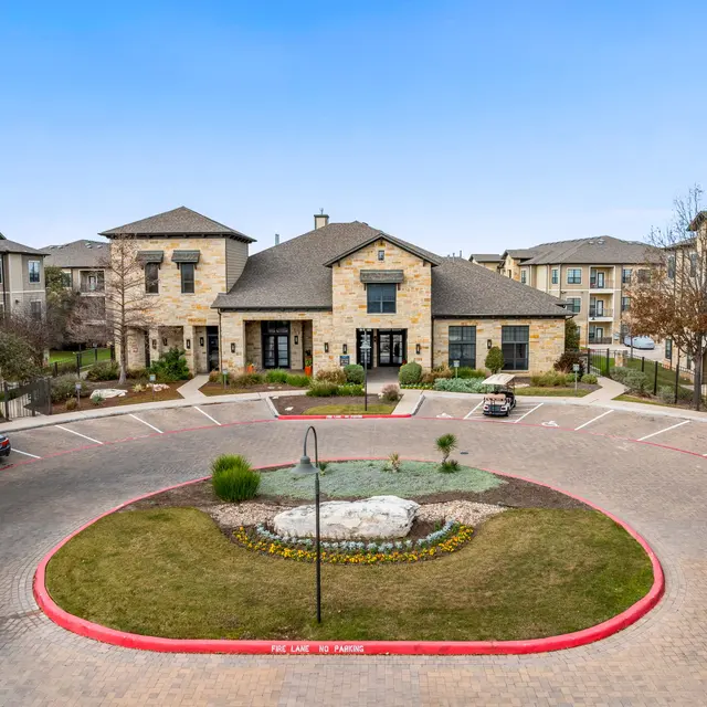 Aerial view of a multi-story apartment complex featuring a central circular drive with landscaped areas and decorative stonework buildings.