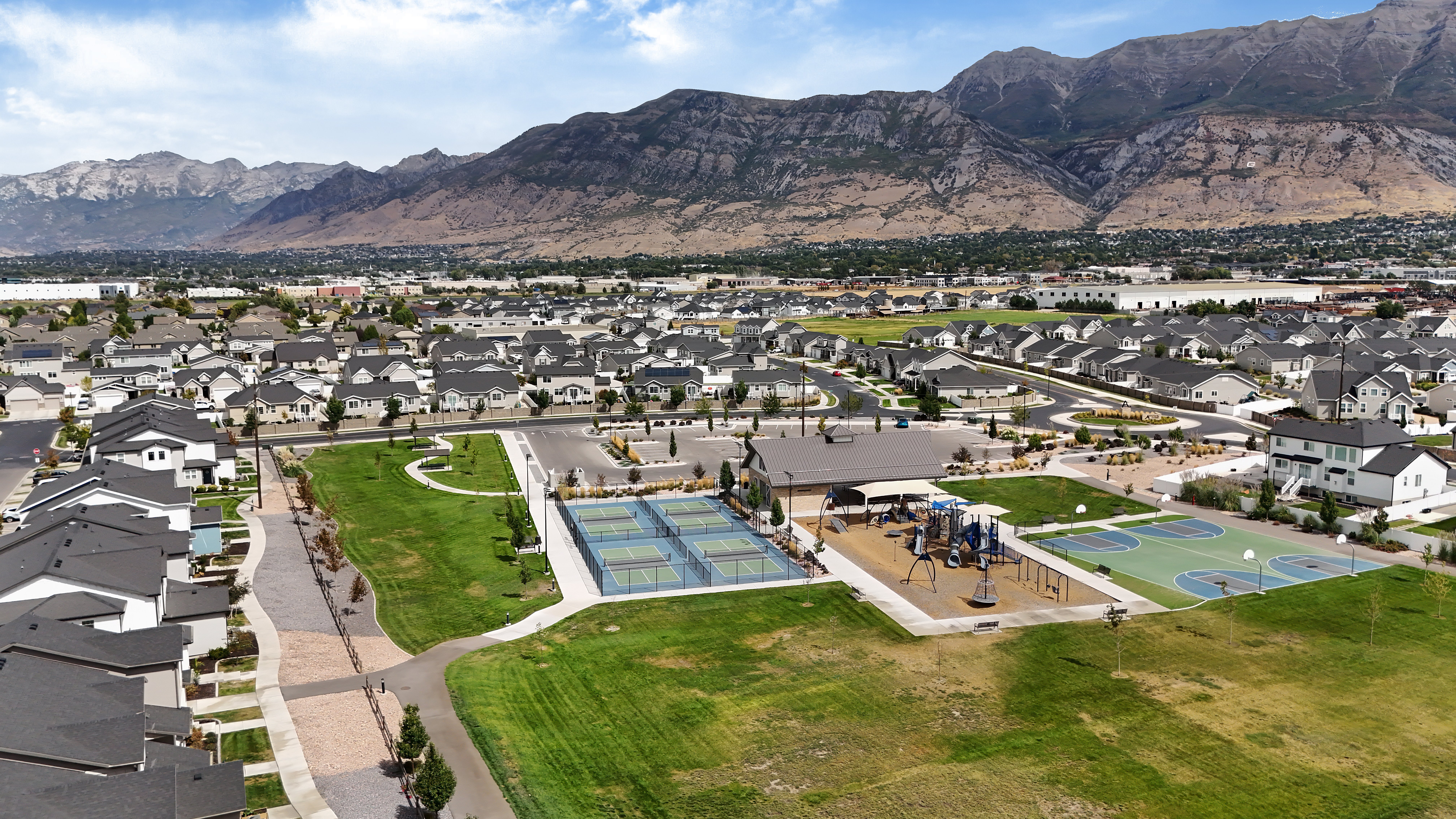 Aerial View of Residential Neighborhood and Park Aerial view of a residential neighborhood featuring houses, a park, tennis courts, playground, and mountains in the background.