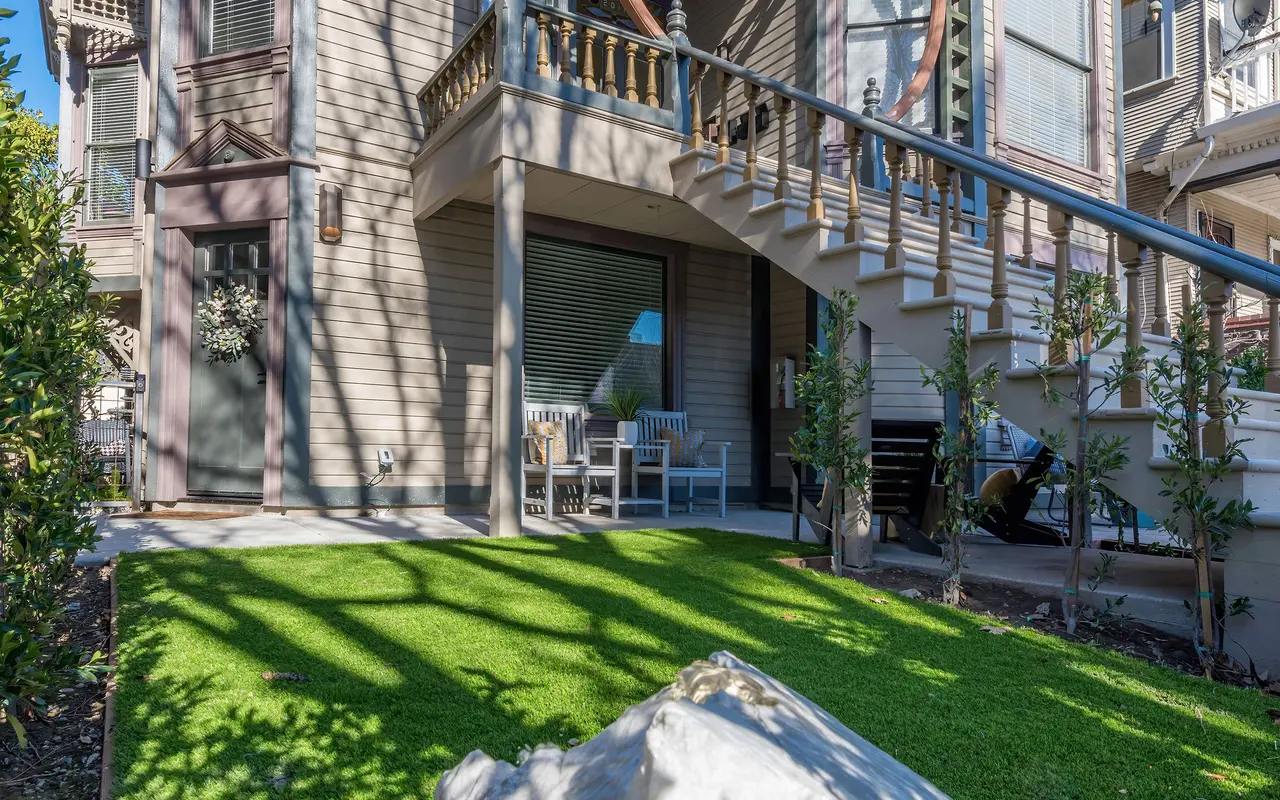 A Victorian-style house with ornate architectural details, a lawn in the forefront, and a rock feature.