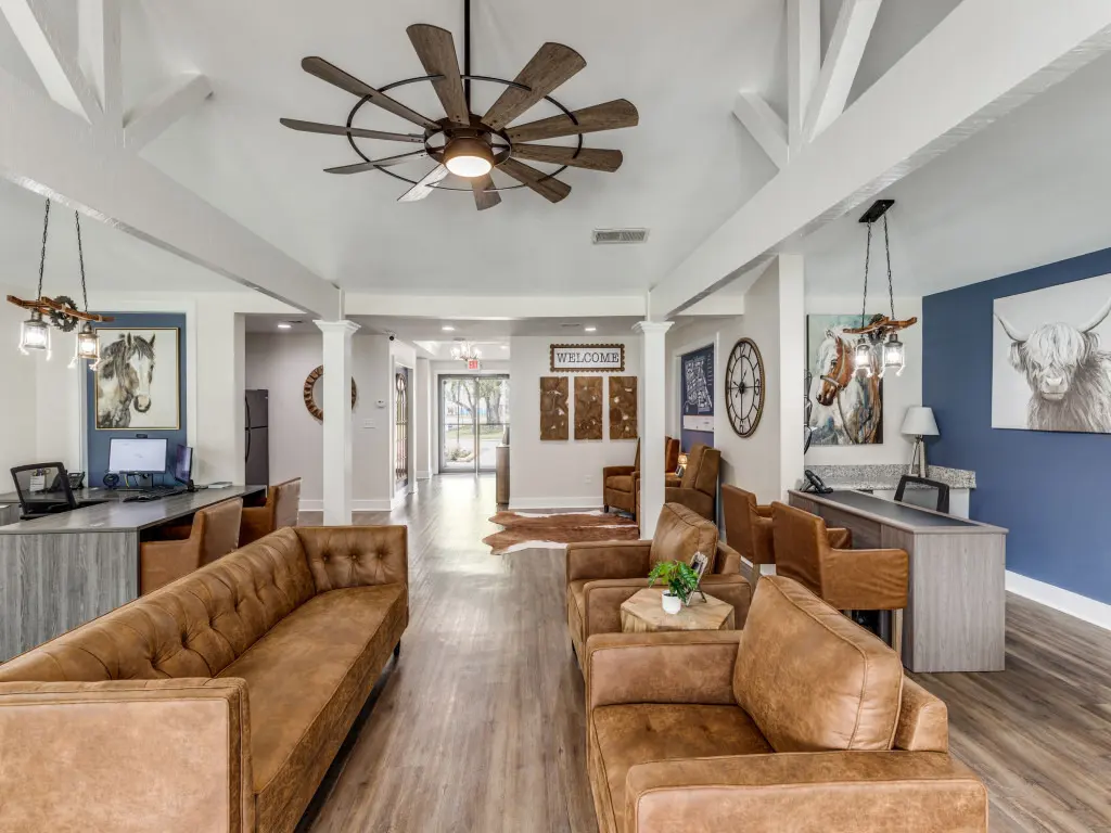 Contemporary Lobby Interior A modern lobby area featuring brown leather sofas, a large ceiling fan, and decorative wall art of animals. The space is bright and inviting with wooden floors and white beams.