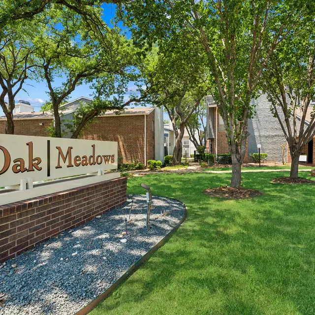 A welcoming entrance sign for Oak Meadows set in a green landscape with trees and well-maintained grounds. The office building is visible in the background.