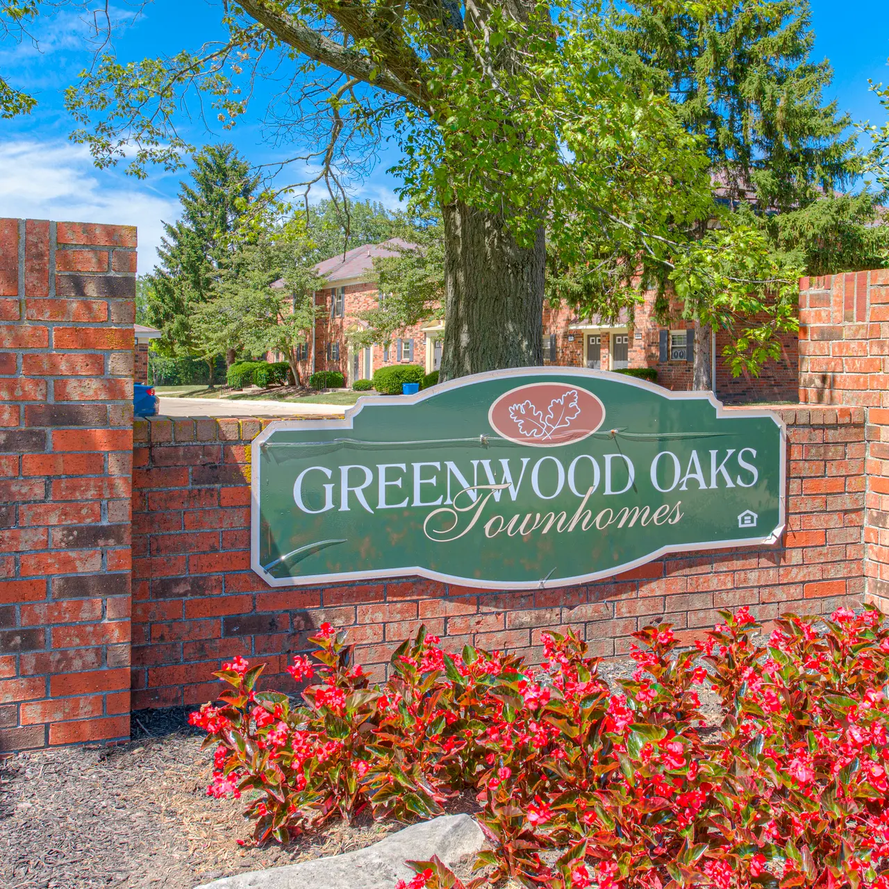 Greenwood Oaks Townhomes Sign Sign for Greenwood Oaks Townhomes with red flowers in the foreground and trees in the background under a blue sky