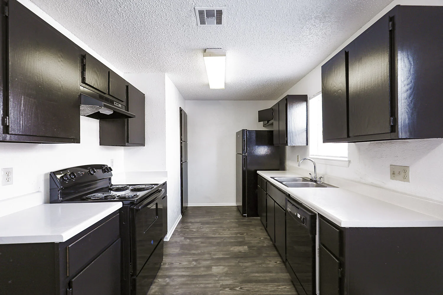 Copper Mill Apartments Modern kitchen with black cabinets, white countertops, a stove, and a sink, featuring vinyl flooring and minimal decor.