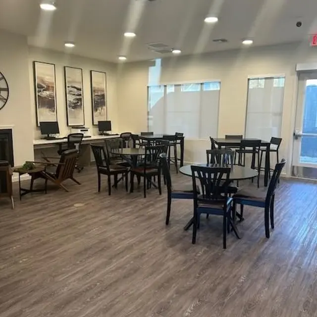 Modern Reception Area A spacious room with multiple round tables and chairs arranged neatly. The flooring is wood-like, and the walls feature large framed artworks. There are windows with light curtains allowing natural light in.