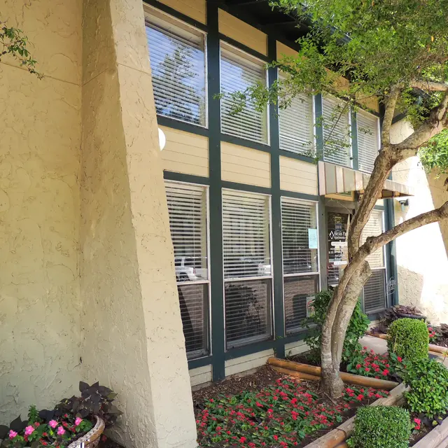 Building Exterior with Landscaping Exterior view of a building featuring large windows, bushes, and trees in the landscaping.