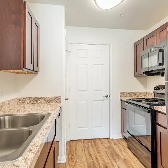 A modern kitchen featuring dark wood cabinets, stainless steel appliances, and a granite countertop with double sinks.