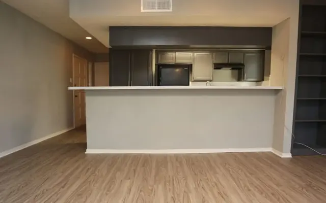 A modern living room area with wooden floors and a kitchen bar counter in the background.