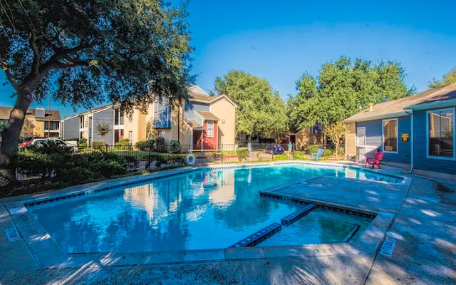 A clear swimming pool surrounded by lush greenery and residential buildings on a sunny day.
