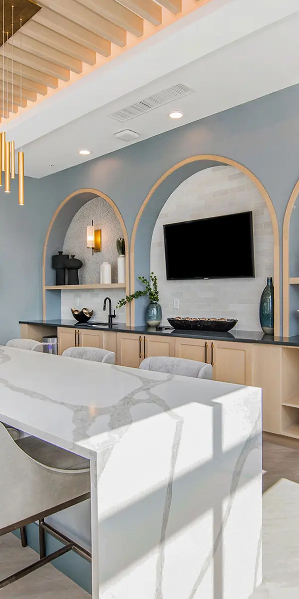 Modern kitchen and dining area with stylish lighting, a long table, and arched wall niches showcasing decorative items.