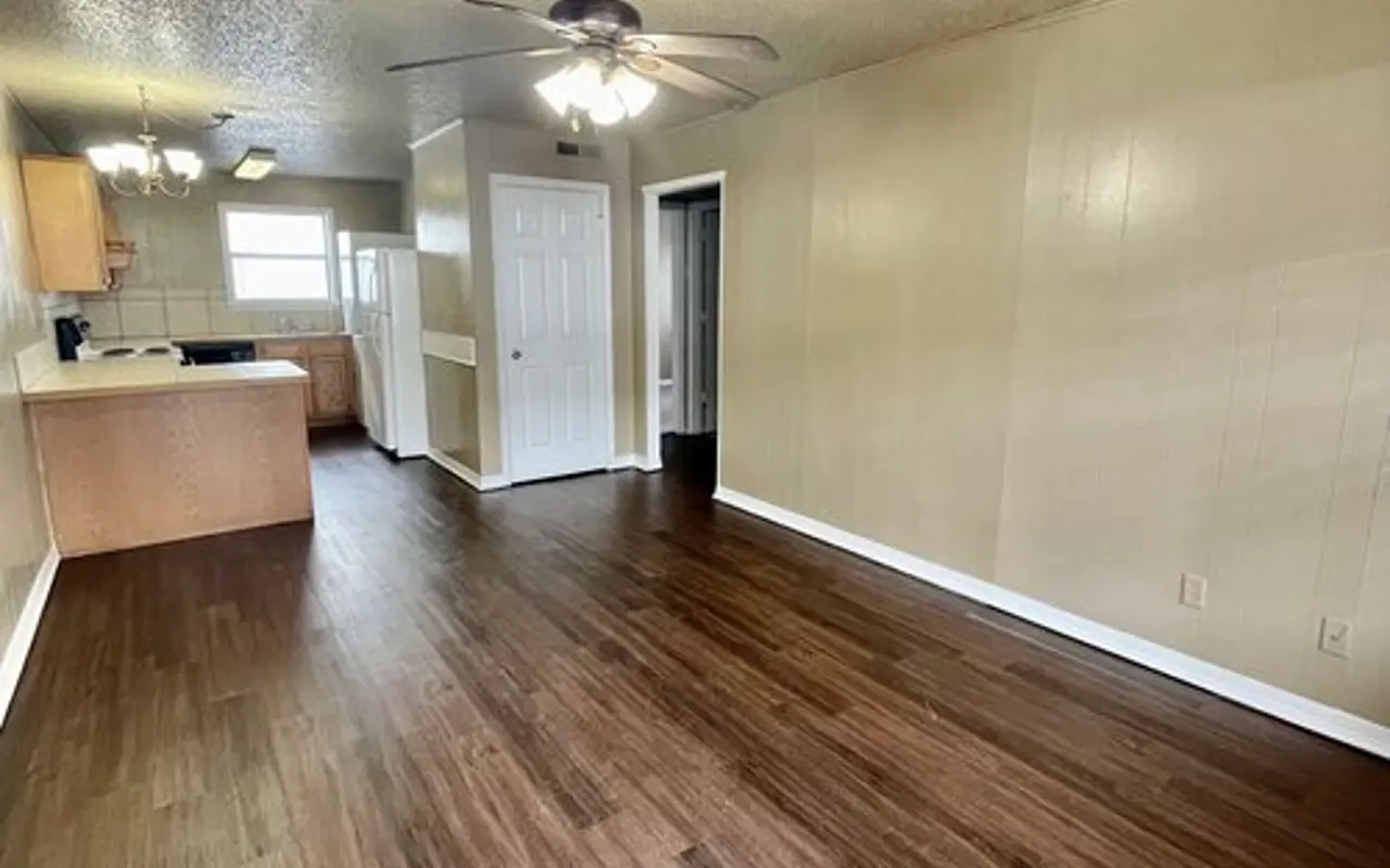 Spacious Living Room with Hardwood Floors An open living room with hardwood floors, ceiling fan, and a view into the kitchen area.