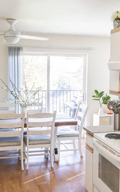 Bright and modern kitchen and dining area with a table and white chairs, a window with a view, and kitchen appliances.