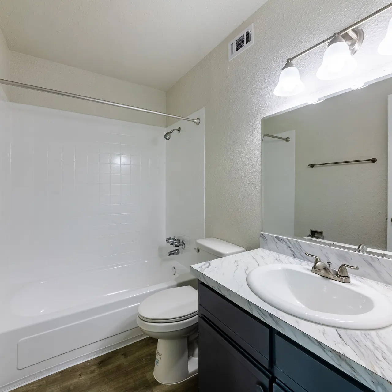 A modern bathroom featuring a bathtub with a shower, a toilet, and a sink with a marble countertop.