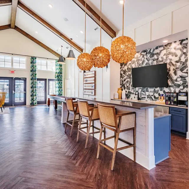 Modern Lobby Design A spacious and modern lobby featuring wooden beams, a stylish bar with woven pendant lights, and a large TV against a patterned wall. Comfortable seating areas are visible with bright curtains and contemporary decor.