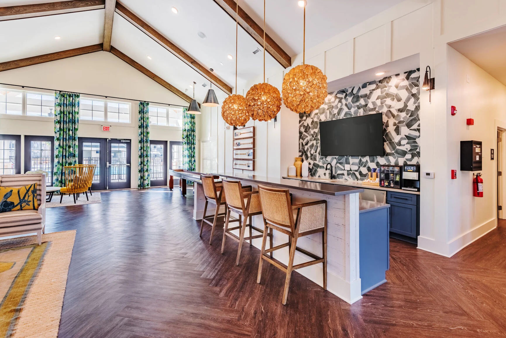Modern Lobby Design A spacious and modern lobby featuring wooden beams, a stylish bar with woven pendant lights, and a large TV against a patterned wall. Comfortable seating areas are visible with bright curtains and contemporary decor.