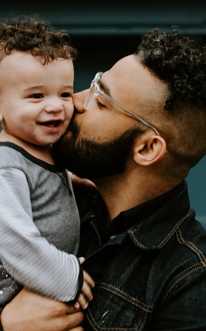 Father and Son Bonding A joyful man kisses his smiling toddler son on the cheek while holding him. The background features a blue garage door.