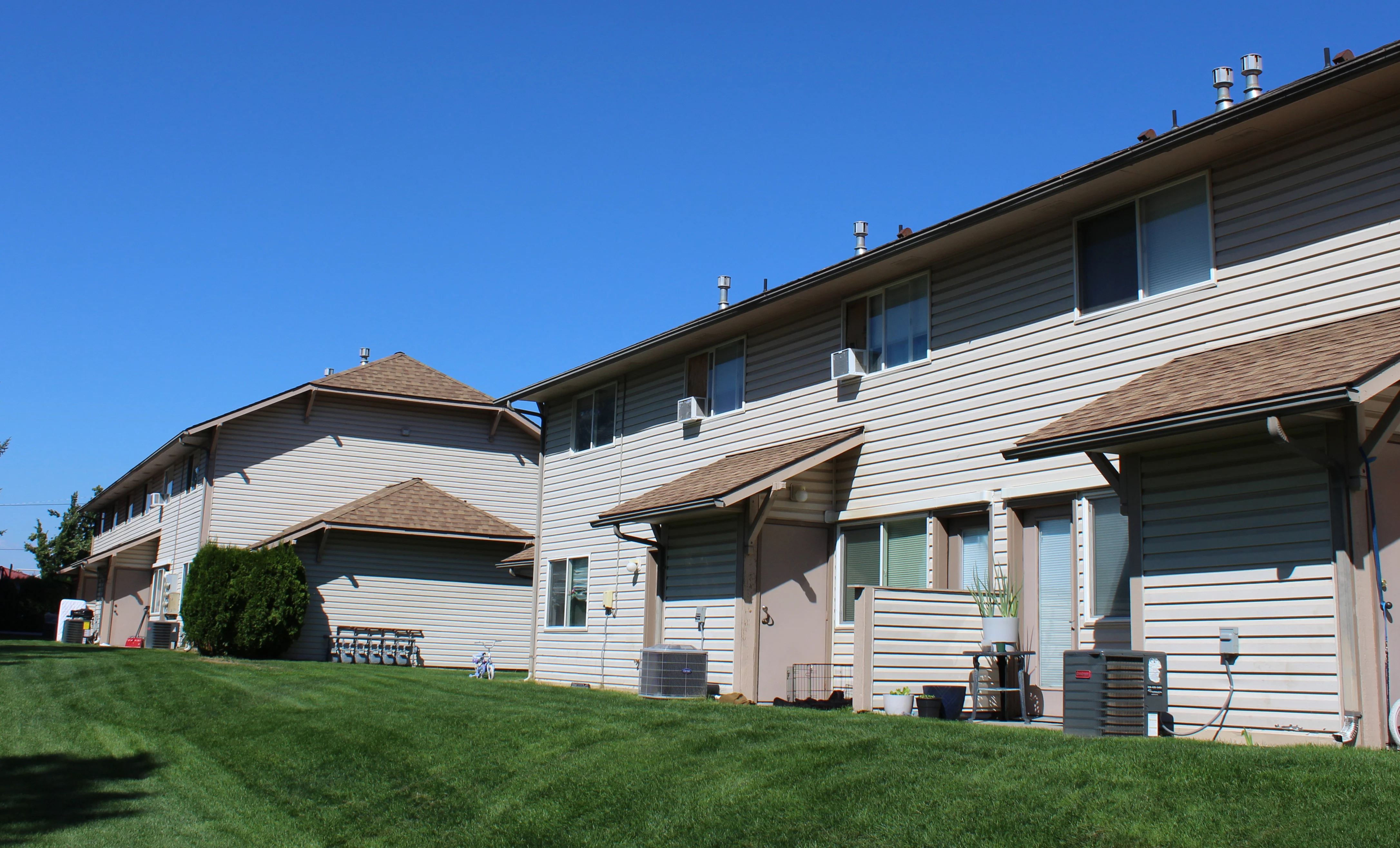 Row of residential buildings with landscaped green lawn under a clear blue sky.