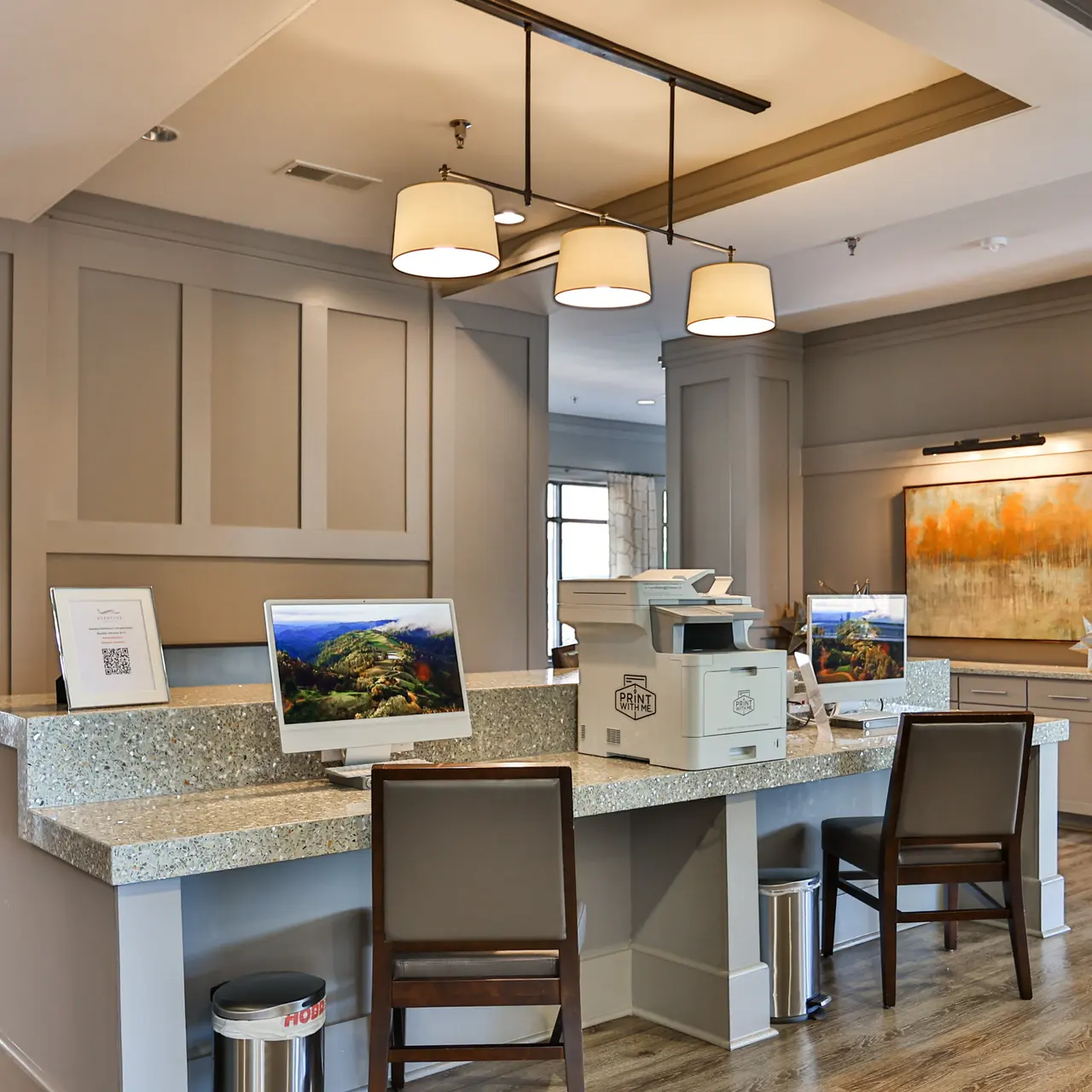 Modern Office Reception Area A modern reception area with beige walls, wooden flooring, and stylish light fixtures. The space features a counter with computers and a printer, surrounded by seating areas and decorative elements.