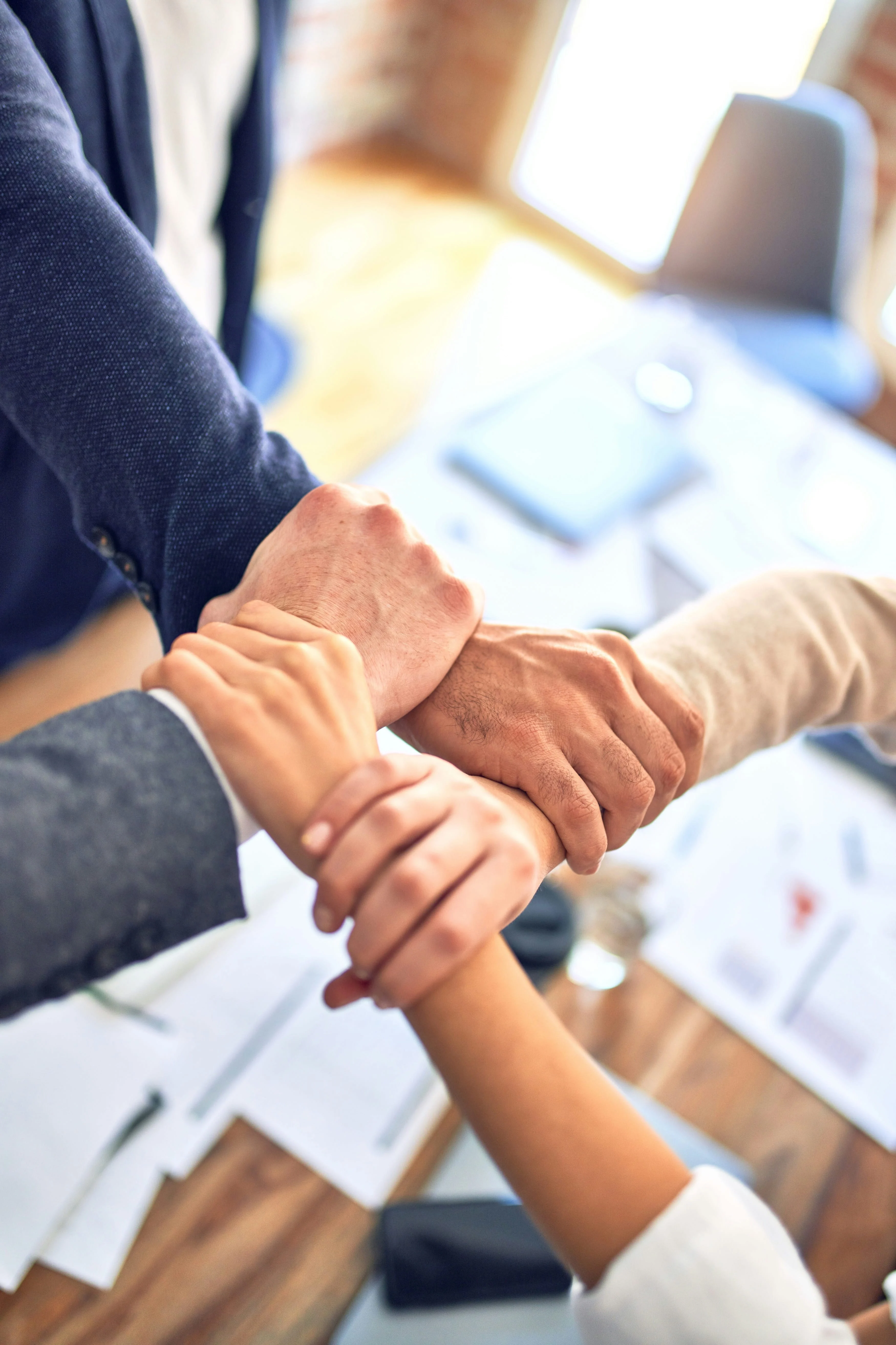 Several hands reaching out to each other in a collaborative gesture above a table with documents and office items.