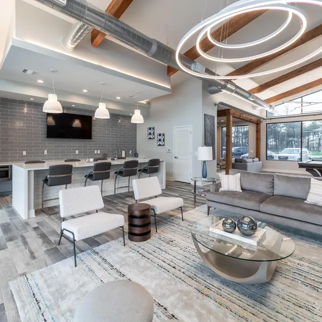 A modern living space with a kitchen area featuring bar stools, a comfortable seating area, and large windows allowing natural light.