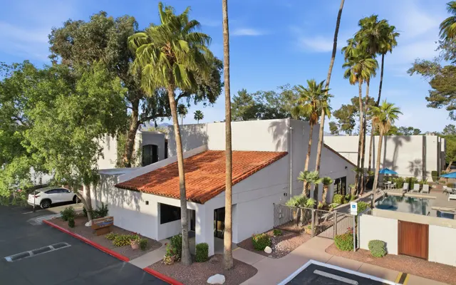 Aerial view of a modern building with a reddish tile roof, surrounded by palm trees and green foliage.