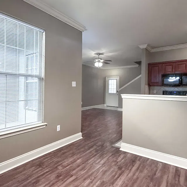 Interior view of a modern living space featuring a wooden floor, large window with blinds, and a kitchen area with red cabinetry.