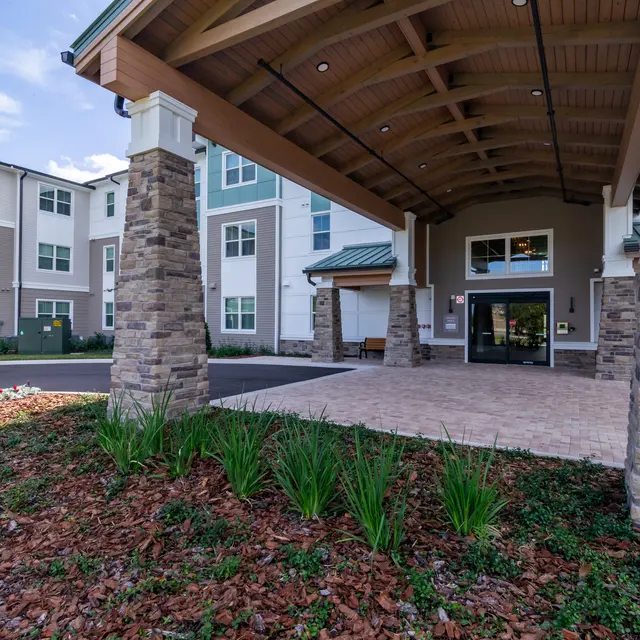 Entrance of a modern apartment complex with stone columns, wooden beams, and landscaped plants.