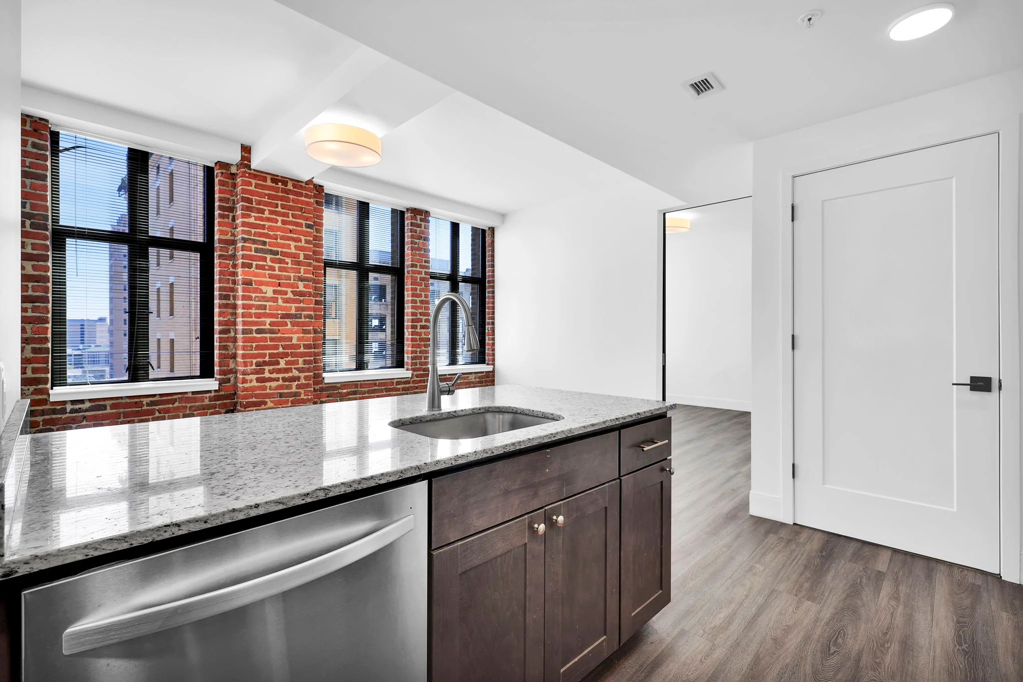 Modern Kitchen with Brick Wall A modern kitchen featuring granite countertops, stainless steel appliances, and large windows with views of a city.