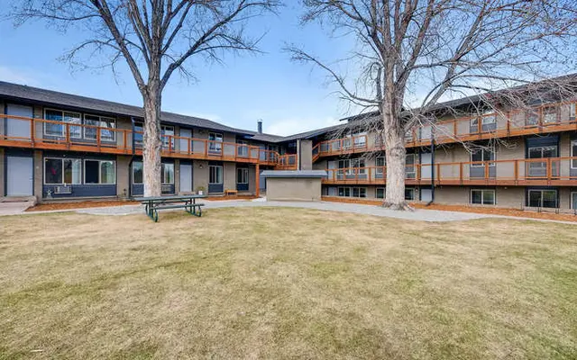 View of an apartment complex featuring multiple levels, with a grassy courtyard and large trees.