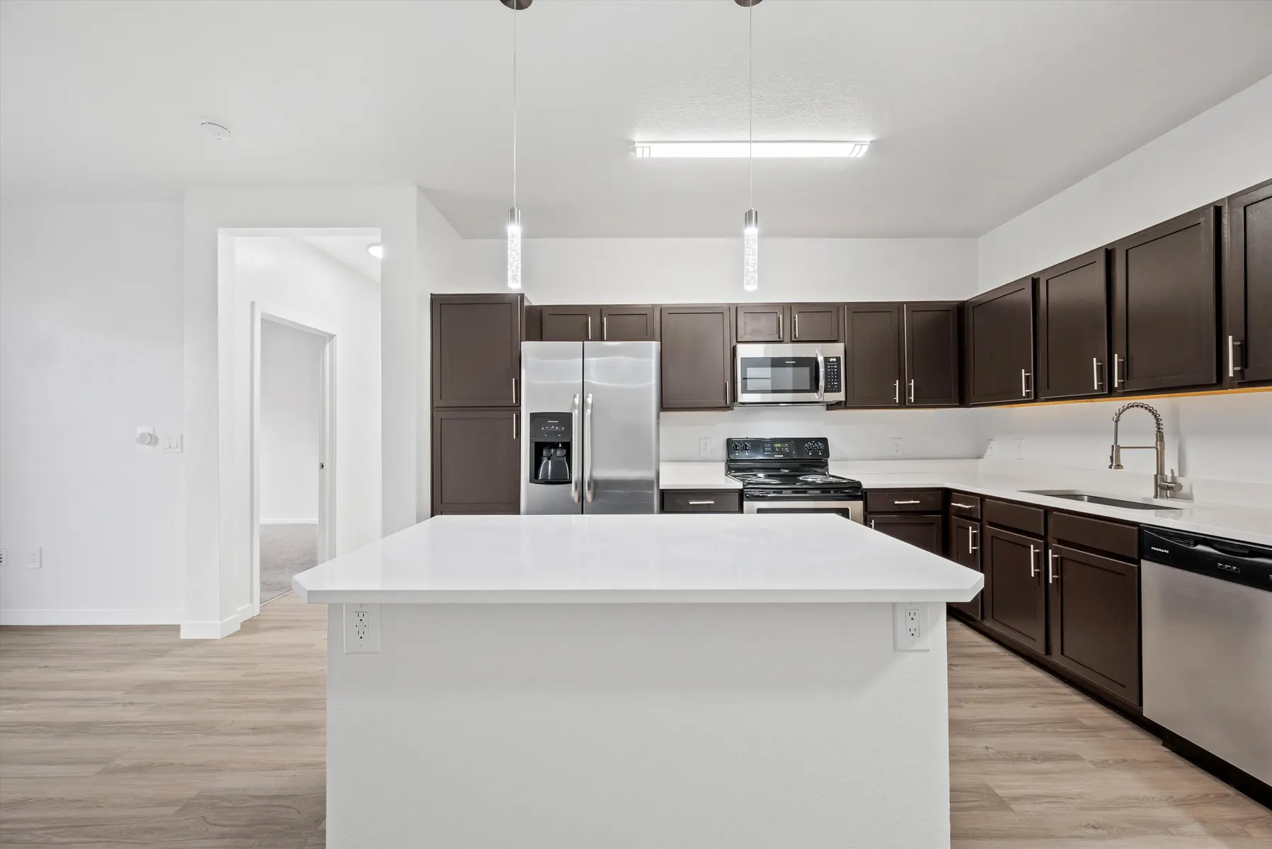 A modern kitchen with dark wooden cabinets, stainless steel appliances, and a large central island with a white countertop.