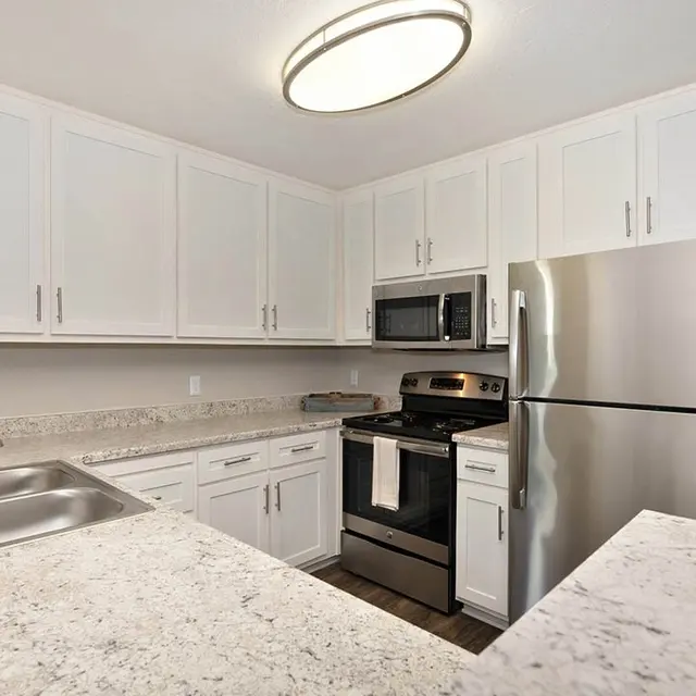 A modern kitchen featuring white cabinetry, stainless steel appliances, and granite countertops. Includes a sink and a view of the adjacent open space.