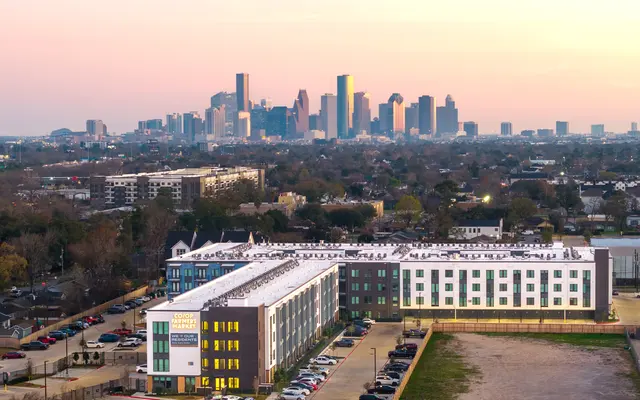 Aerial view of a modern residential building in the foreground with a city skyline in the background during sunset.