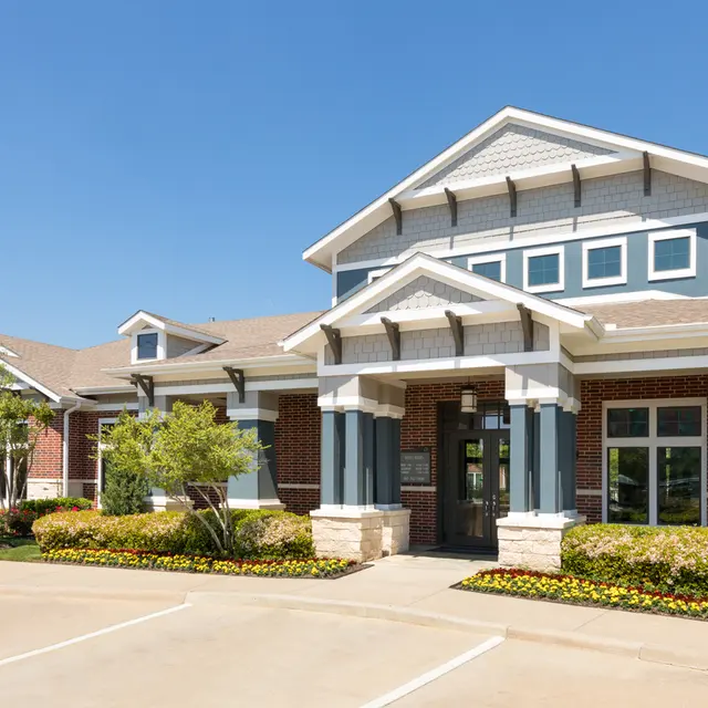 A modern building facade with a welcoming entrance, surrounded by well-maintained landscaping and clear blue skies.