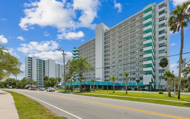Modern apartment buildings along a road with palm trees and a clear blue sky.
