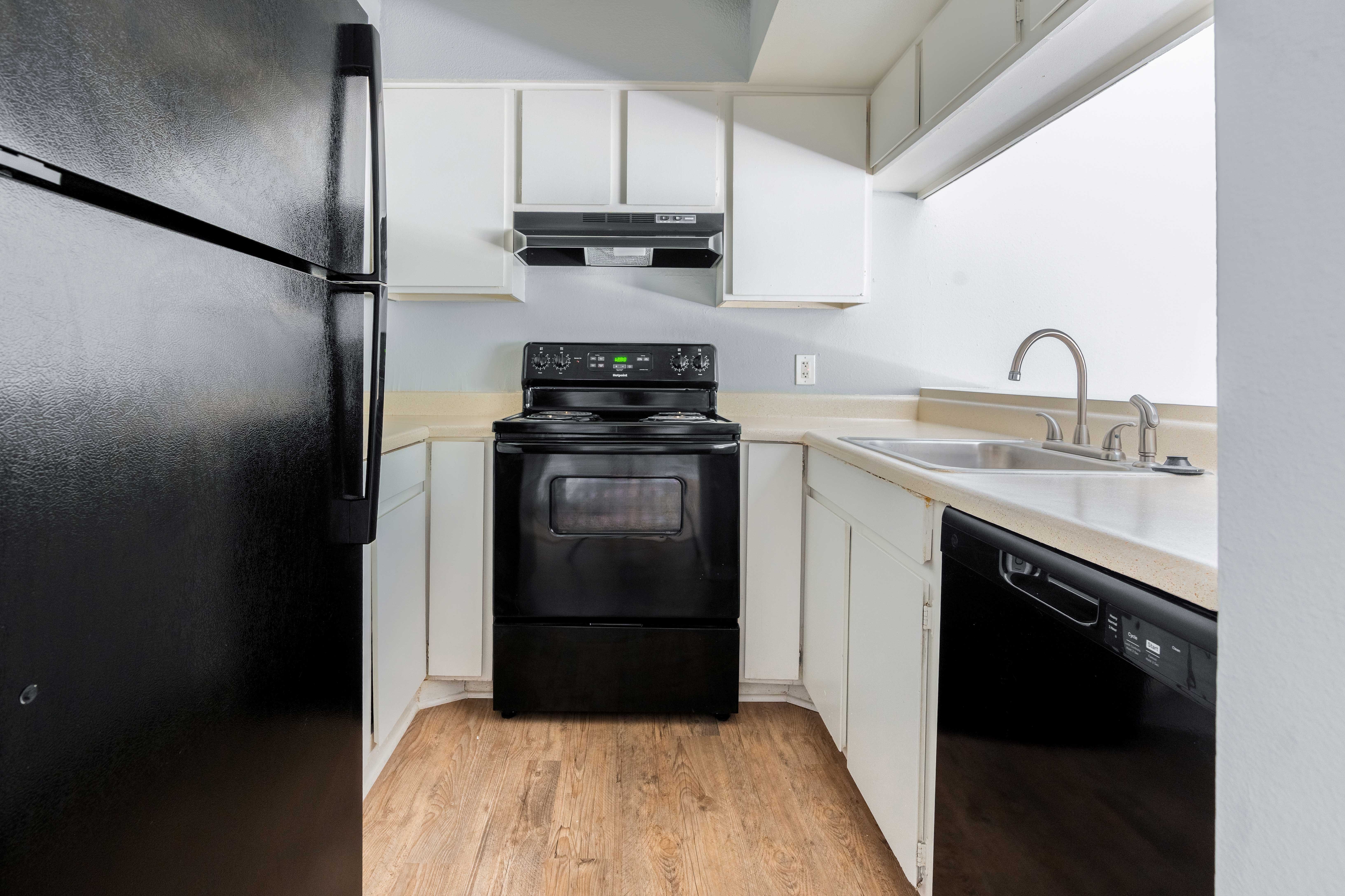 A small, modern kitchen featuring black appliances, white cabinets, and wooden flooring.