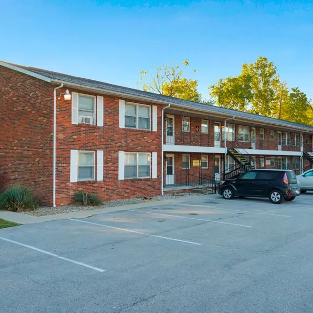 Exterior view of a two-story brick apartment building with a parking lot in front