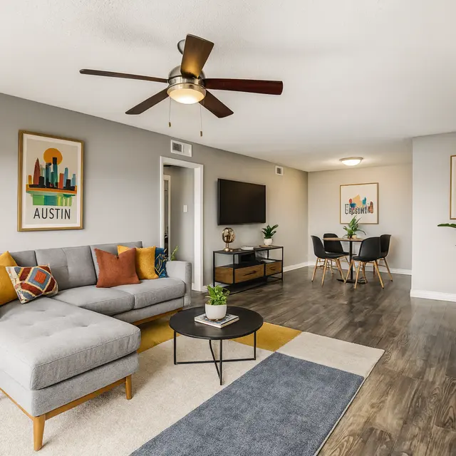 A modern living room featuring a gray sectional sofa, coffee table, potted plants, and wall art depicting the word 'Austin'.