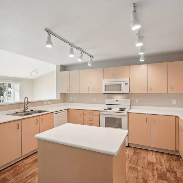 Modern kitchen featuring light-colored cabinets, a central island, and stainless steel appliances. Natural light floods the space through large windows.