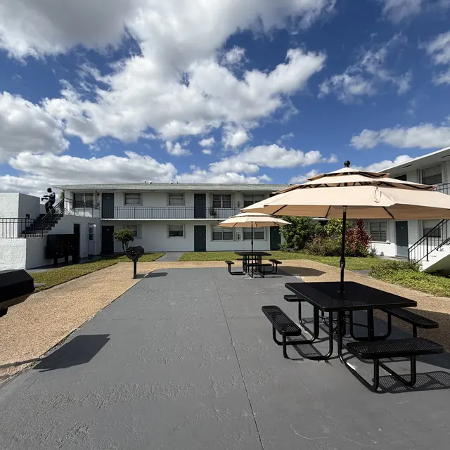 Outdoor seating area with picnic tables and umbrellas in an apartment complex.