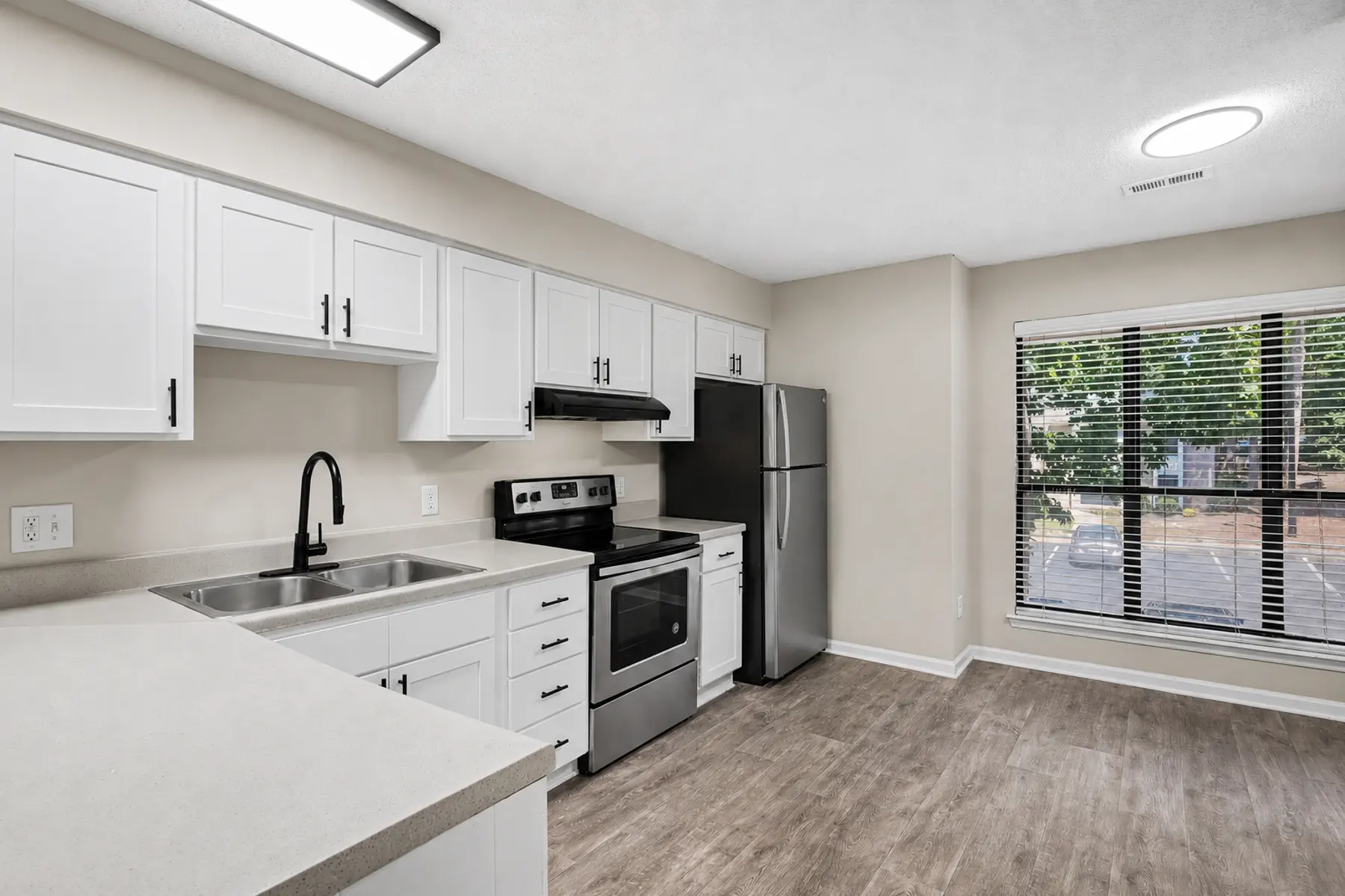 A modern kitchen featuring white cabinets, stainless steel appliances, and a large window with blinds letting in natural light.