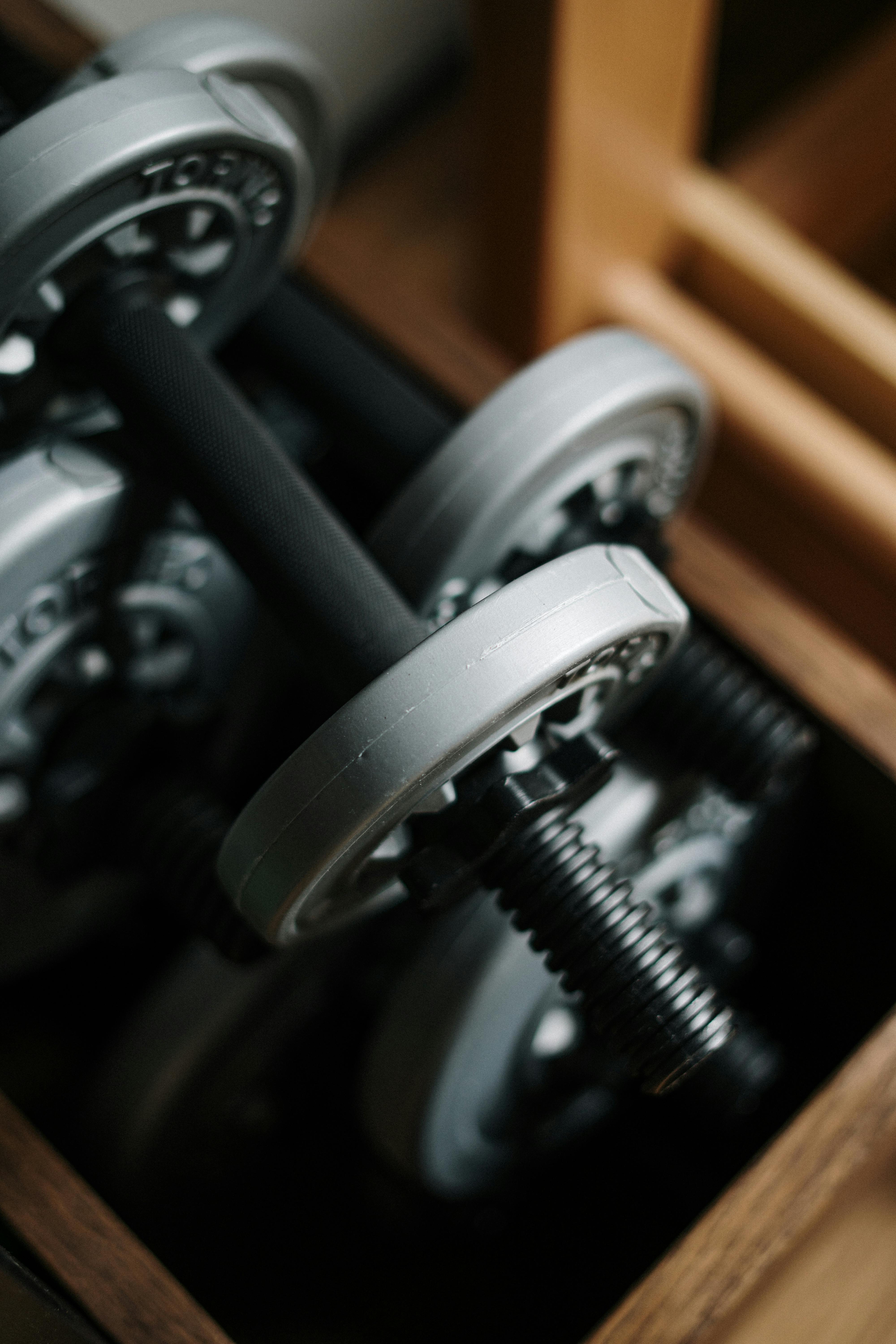 Neatly Stored Dumbbells A close-up view of several dumbbells stored in a wooden box, showcasing the metallic plates and handles.