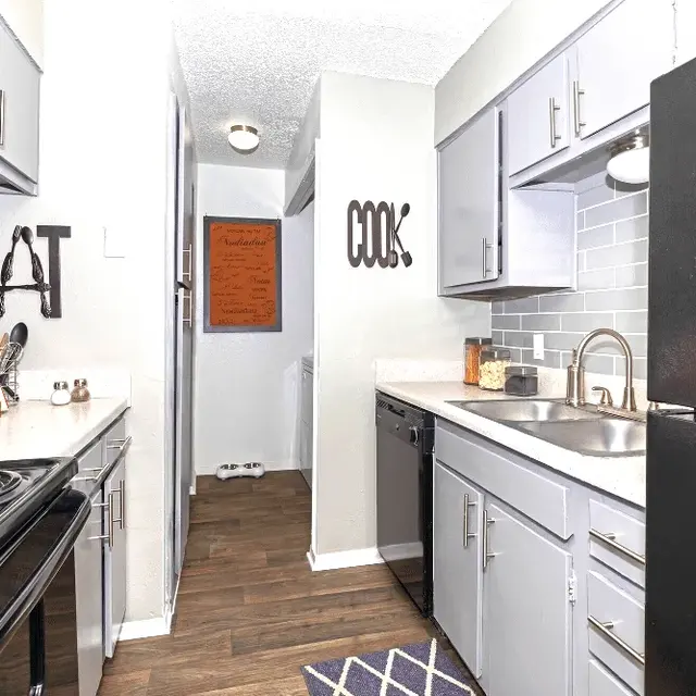 A modern kitchen featuring sleek gray and black cabinetry with stainless steel appliances. Decorative signs that read 'EAT' and 'COOK' are mounted on the wall. A wooden floor complements the overall design.
