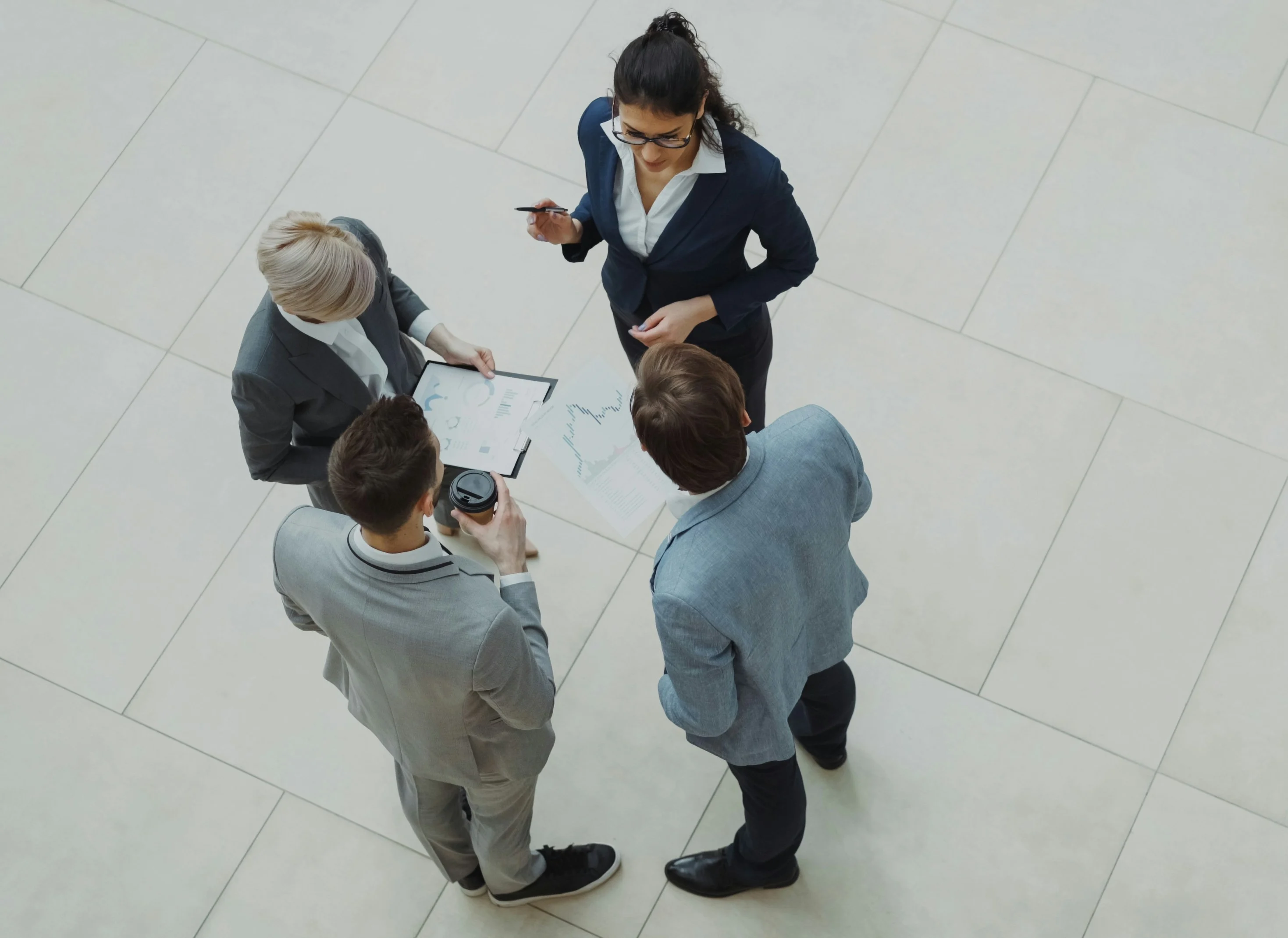 Collaborative Business Meeting Four business professionals engaged in discussion, standing around a table with documents and a coffee cup