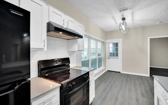 A modern kitchen featuring white cabinetry, black appliances, and large windows with blinds.