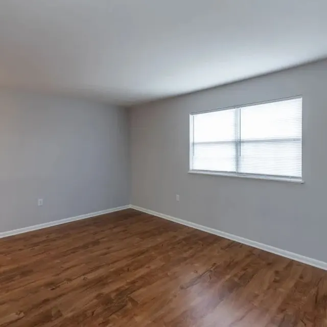 An empty room featuring a wood floor and a window with blinds.