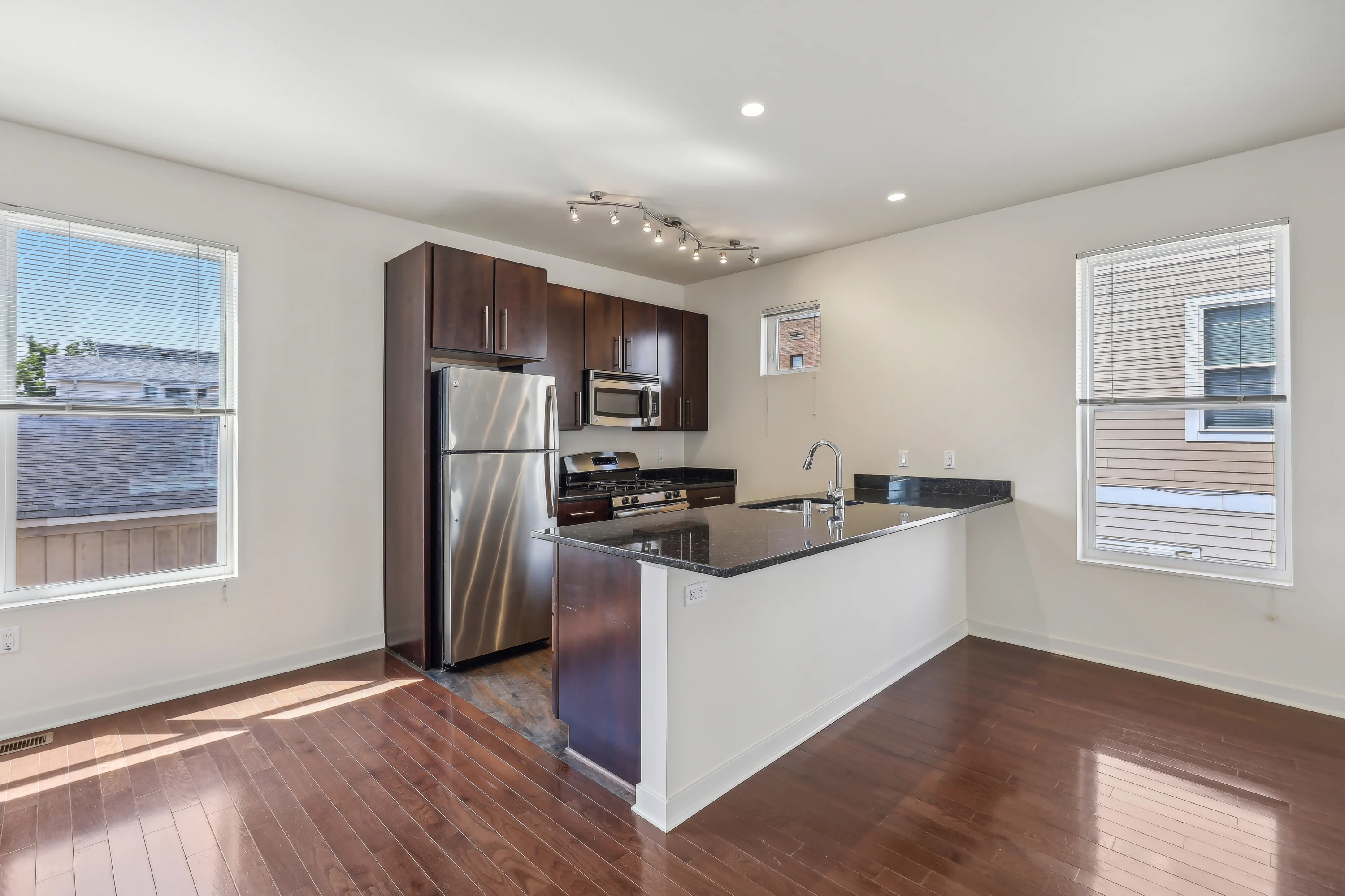 A contemporary kitchen with dark wood cabinets, stainless steel appliances, and a large island. The space features hardwood flooring and plenty of natural light from multiple windows.