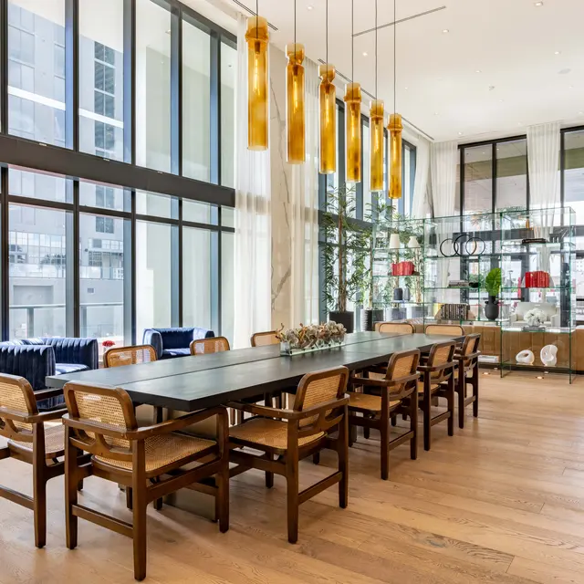 A spacious modern dining area with a long table and wooden chairs, large windows allowing natural light, and decorative pendant lights overhead.