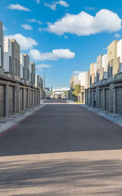 Modern Townhouse Row A row of modern townhouses with garage doors aligned along a street under a clear blue sky with fluffy clouds.